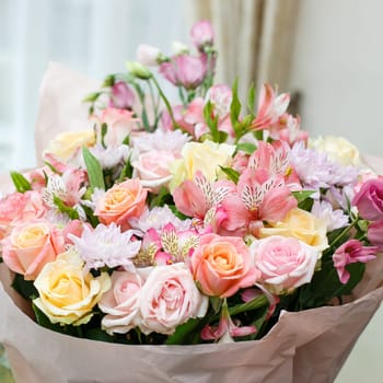 Large festive bouquet of fresh flowers made in pink stands on the table. Bouquet in a paper wrapper and tied with a pink ribbon. Concept of giving flowers for a birthday or wedding.