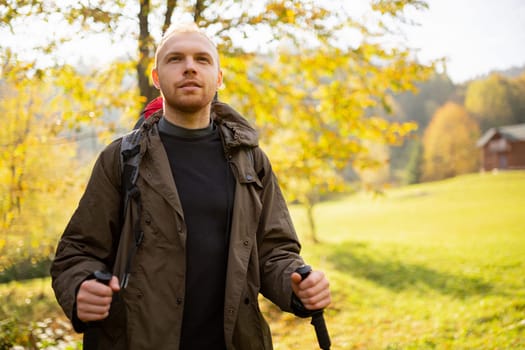 Close up portrait of a tourist man who travels in the mountains and rejoices when he sees his goal in the distance. Man with trekking sticks stands on a background of autumn mountain nature. Blurred.