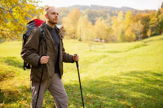 Portrait of a male adventurer hiking in the mountains with a backpack and trekking sticks in his hands standing on a mountain and looking to the side. Hiking. Banner. Place for advertising or text.