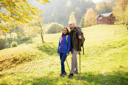 Portrait of a couple of young hikers with backpacks and trekking stick on a background of mountain countryside. Concept of hiking, tourism, nature, people and lifestyle.