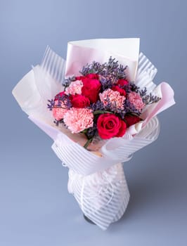 Bouquet of red and pink flowers wrapped in festive paper on a blue background. Festively packed bouquet in red and purple colors. Concept of Women's Day, Mother's Day and Birthday.