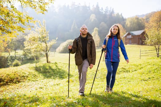 Man and a woman with backpacks on their shoulders and with trekking poles go hiking in the mountains. Couple leads an active and healthy lifestyle together. Concepts about travel and wanderlust.