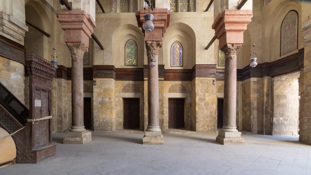 Interior of Sultan Qalawun public historic mosque with stone columns, colored stained glass windows and wooden doors, Cairo, Egypt