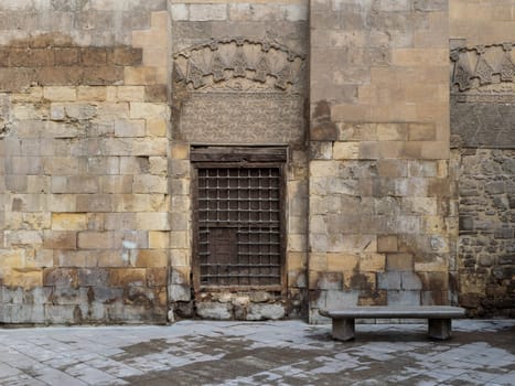 Wooden window with decorated iron grid over stone bricks wall and marble garden bench, Moez Street, Cairo, Egypt