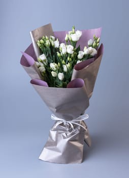 Large festive bouquet of white eustoma stands on a blue background. Flowers are wrapped in double-sided paper and tied with ribbon. Concept of Women's Day, Mother's Day and Birthday.