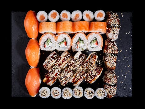 Japanese oriental cuisine. Top view of a large set of sushi on a black stone board. Lots of different maki, nigiri and rolls. Concept of delivery of delicious original sushi sets.