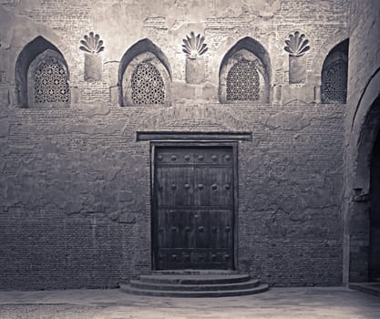 Aged wooden weathered door, perforated arched stucco window decorated with floral patterns, and three steps on stone bricks wall, Ibn Tulun Mosque, Cairo, Egypt
