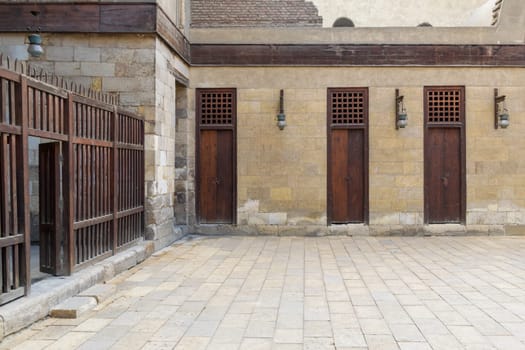 Three adjacent doors in a stone bricks wall and wooden fence at the main courtyard of public historic mosque of Sultan Al Nassir Qalawun, Cairo, Egypt