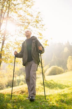 Natural background. View from below of a young male traveler with trekking sticks in his hands standing in the sun. Smiling man enjoys the beauty of nature. Concepts of travel and wanderlust.