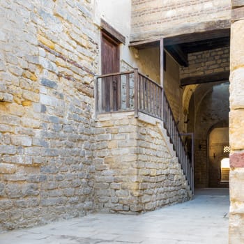 Exterior daylight shot of old abandoned staircase with wooden balustrade and wooden door at stone bricks passage surrounding Sultan Qalawun Complex located in Al Moez Street, Cairo, Egypt