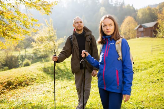 Portrait of a beautiful male traveler with a backpack and trekking stick traveling with his wife in the autumn mountains. Concept of active tourism. Selective focus. Banner.