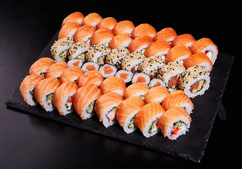 Large set of sushi roles consisting of many California and Mackie roles. Sushi with fresh stuffing on a black stone plate.