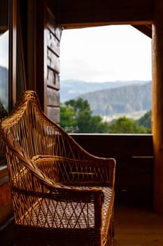 Beautiful brown wicker chair on the terrace of a wooden cottage overlooking the mountain forest. Blurred background. Leisure concept.