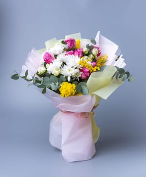 Delicate holiday bouquet wrapped in bright floral paper on a blue background. Beautifully packaged flower arrangement with roses, yellow flowers, white chrysanthemums and eucalyptus twigs.