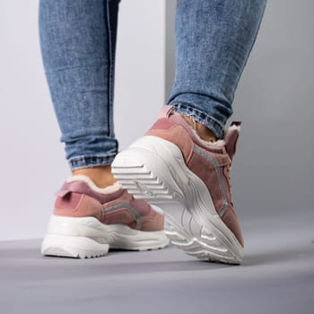 Close up demonstration of rear view of female model in warm sneakers with down inside. Comfortable white and pink sneakers on woman's legs in jeans. Selective focus.