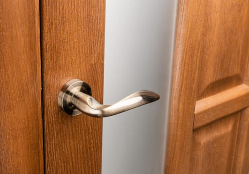 External door handle without protective lock on wooden frame. Close up of metallic door handle on brown front or interior door. Home door design choice concept.