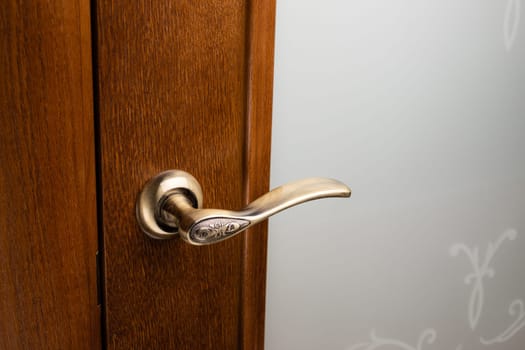 External door handle without protective lock on wooden frame. Close up of gold door handle on brown front or interior door. Home door design choice concept.