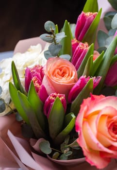 Close up of bright pink roses and tulips folded in one bouquet and wrapped in floral paper. Concept of floral arrangements for greetings. Selective focus. Place for text.