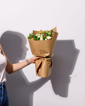 Unknown woman holds bouquet of fresh flowers on white background. Copy space advertising layout. Shadow of woman and flowers on wall. Valentines day, women's day or birthday concept.
