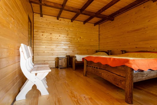 Small bedroom with two wooden beds, chairs and bedside tables in a modern cottage with wooden walls. Handmade furniture.