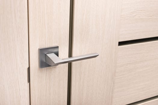 Close up of chrome gray metal door handle on light interior door. Stylish light beige door with small inserts of black frosted glass. Concept of catalog of door handles for furniture store.