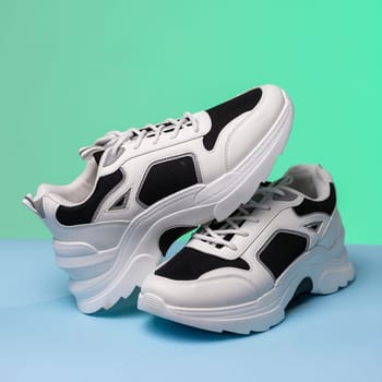 Details. Close up of black and white sports shoes on colored background. One sneaker rests on another standing on blue and green background. Sports shoe store concept. Banner. Copy space.