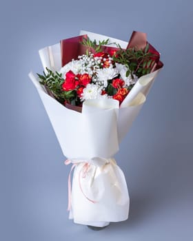 White and red flowers wrapped in bright floral paper on a blue background. Festively packed bouquet of pink roses, white chrysanthemums, gypsophila and sprigs of greenery.
