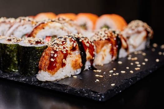 Japanese traditional cuisine. Close up of delicious sashimi sushi with tuna drizzled with soy sauce, sprinkled with sesame seeds and lying on a black board.