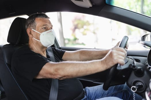 Senior in his 70s driving a car wearing face mask for protection against corona virus