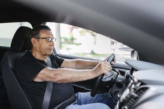 Happy senior in his 70s driving a car