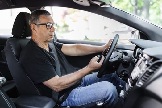 Active senior in his 70s driving a car and usig his mobile phone