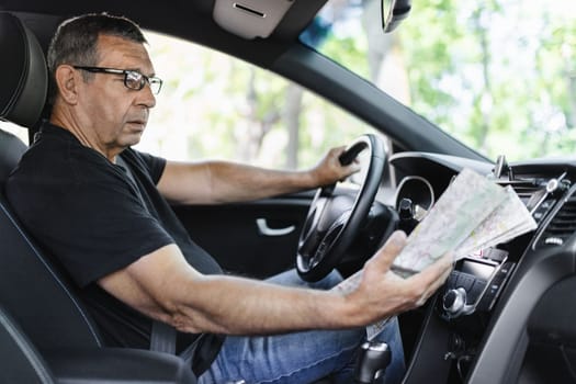 Senior behind the steering wheel of a car, looking at map for directions