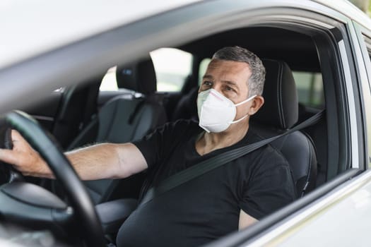 Senior in his 70s driving a car wearing face mask for protection against corona virus