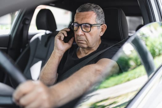 Active senior in his 70s driving a car and usig his mobile phone
