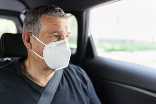 Senior in his 70s sitting at the back of car wearing a face mask for protection against corona virus