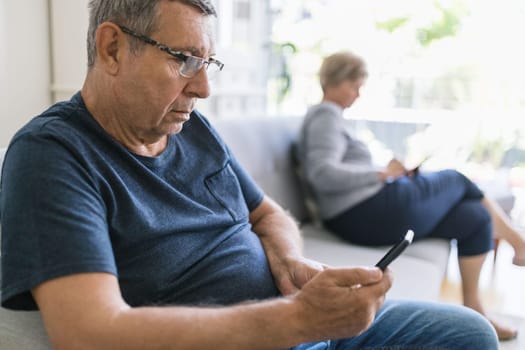 Senior couple sitting on couch and using their mobile phones at home