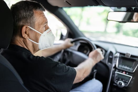 Senior in his 70s driving a car wearing face mask for protection against corona virus