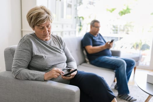 Senior couple sitting on couch and using their mobile phones at home