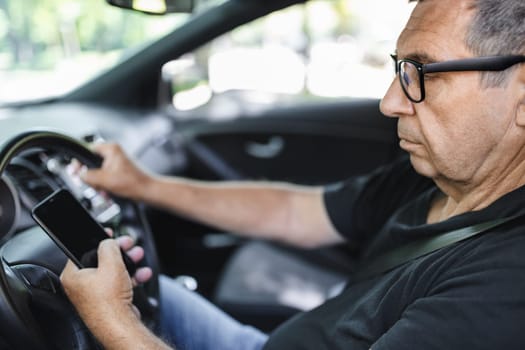 Active senior in his 70s driving a car and usig his mobile phone