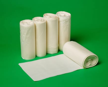 Five rolls of biodegradable eco plastic white garbage bags on green background. New unused rolls of garbage bags for home use. Zero waste lifestyle concept. Advertising banner. Close up.