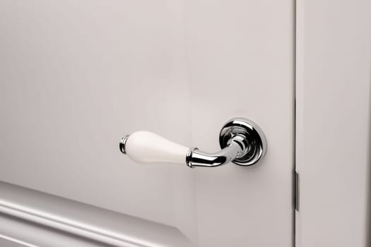 Close up of stylish and elegant door knob or handle on white door. Vintage white and silver door handle on door that is suitable for refined home interior. Details concept.