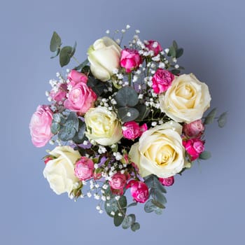 Close up top view of floral arrangement on blue background. Original bright bouquet with beige and pink roses, white gypsophila and eucalyptus twigs. Wedding concept.
