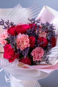 Close up of a bouquet of red and pink flowers wrapped in festive paper on a blue background. Festively packed bouquet in red and purple colors. Concept of floral arrangements for greetings.