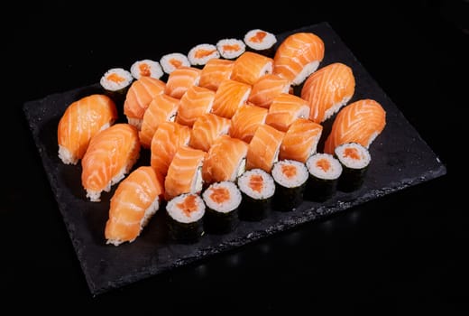 Big set of sashimi rolls with salmon, rolls California and Maki on a black flat board. Concept of delivery of delicious original sushi sets.