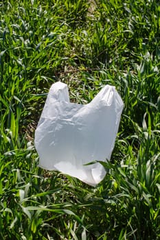 Stop using plastic products. Close up shot on green grass lies white biodegradable bag which is alternative to regular plastic bags. Ecology problems and environmental pollution concept.