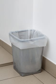 Close up of metal gray trash can with white garbage bag inside. Empty garbage bucket in house, office corridor or in any other room. Waste paper bin concept.