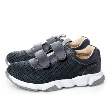 Pair of small sports shoes for boys isolated on white background. Side view of black children's sneakers with velcro and white sole. Concept of comfortable shoes for children.