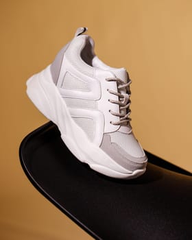 One white women's sneakers on black podium on beige background. Side view close up of new collection of sports shoes on studio background. Advertising banner. Copy space.