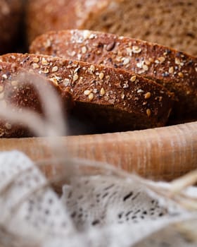 Slices of fresh wholemeal bread with baked crust and various cereals. Close up of homemade bread with sesame seeds lying in clay bowl. Bakery concept. Food background. Selective focus.