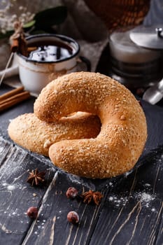 Country home lifestyle. Close up of big sweet bagel on dark rustic wooden table. Crescent-shaped bagels lie near fragrant spices on background of cinnamon sticks and coffee in enamel mug.